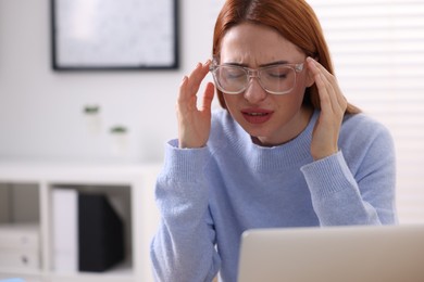 Photo of Woman in glasses suffering from headache at workplace in office, space for text