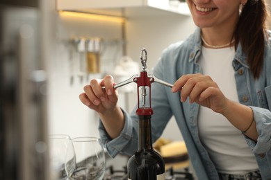 Photo of Smiling woman opening wine bottle with corkscrew indoors, closeup