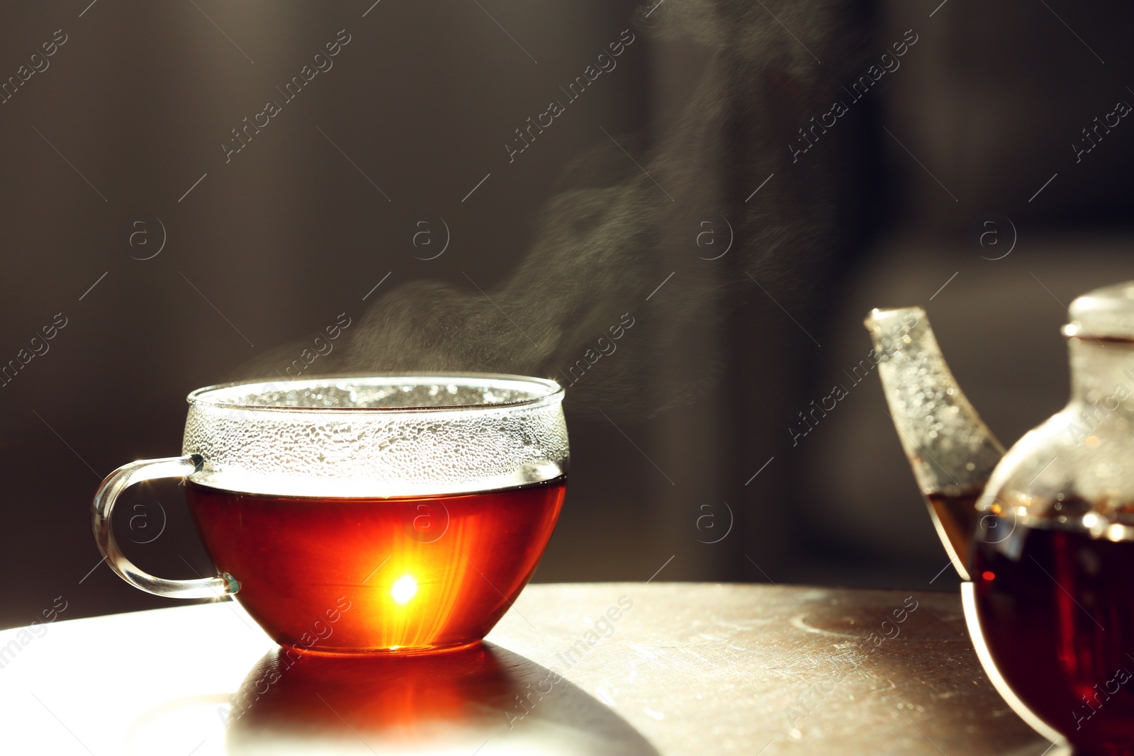 Photo of Teapot and cup of fresh hot tea on wooden table against blurred background