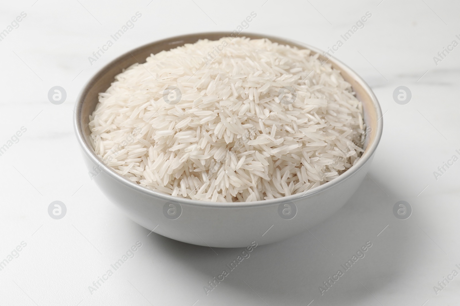 Photo of Raw basmati rice in bowl on white marble table