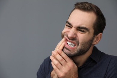 Young man suffering from strong tooth pain on grey background, space for text