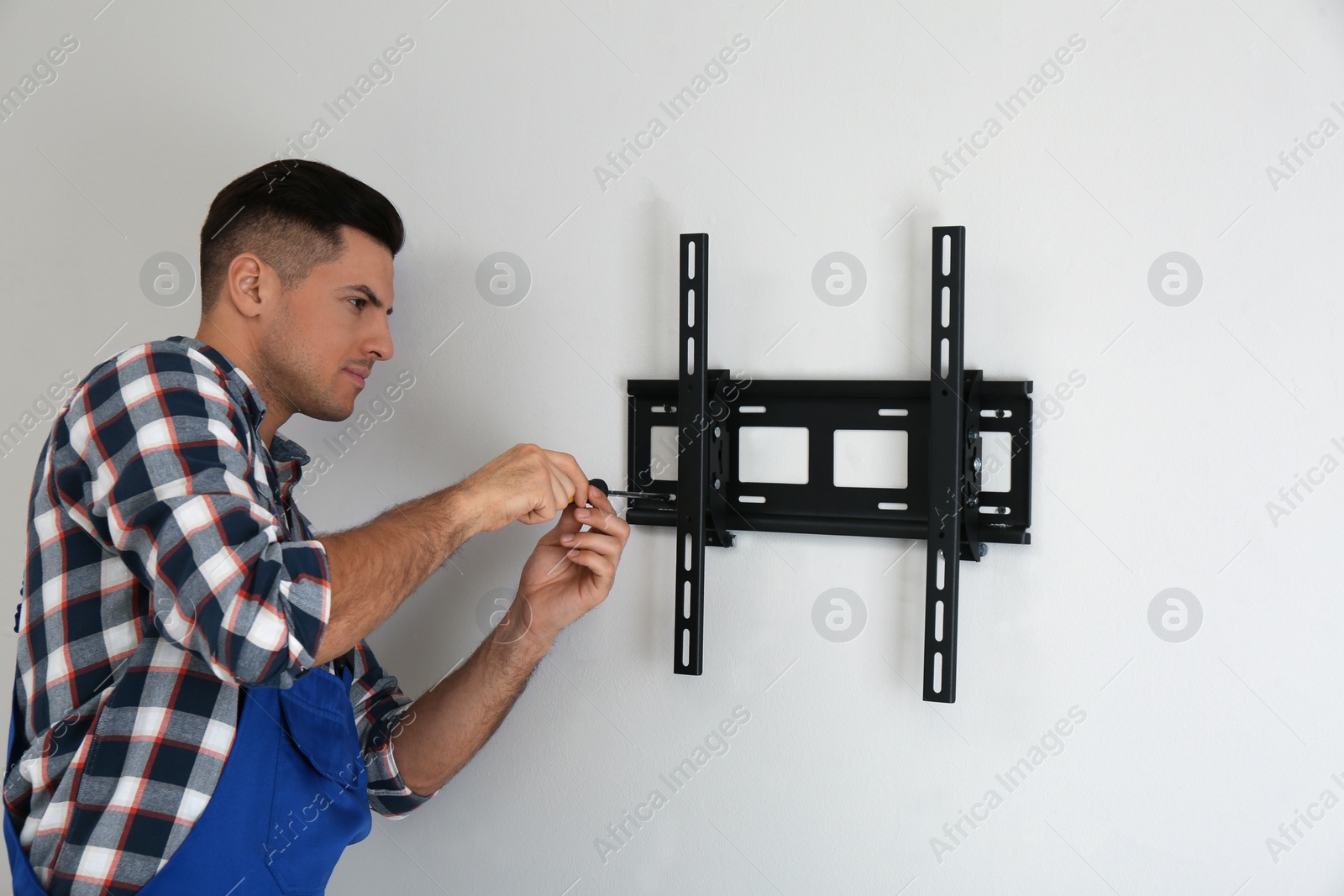 Photo of Professional technician with screwdriver installing TV bracket on wall indoors