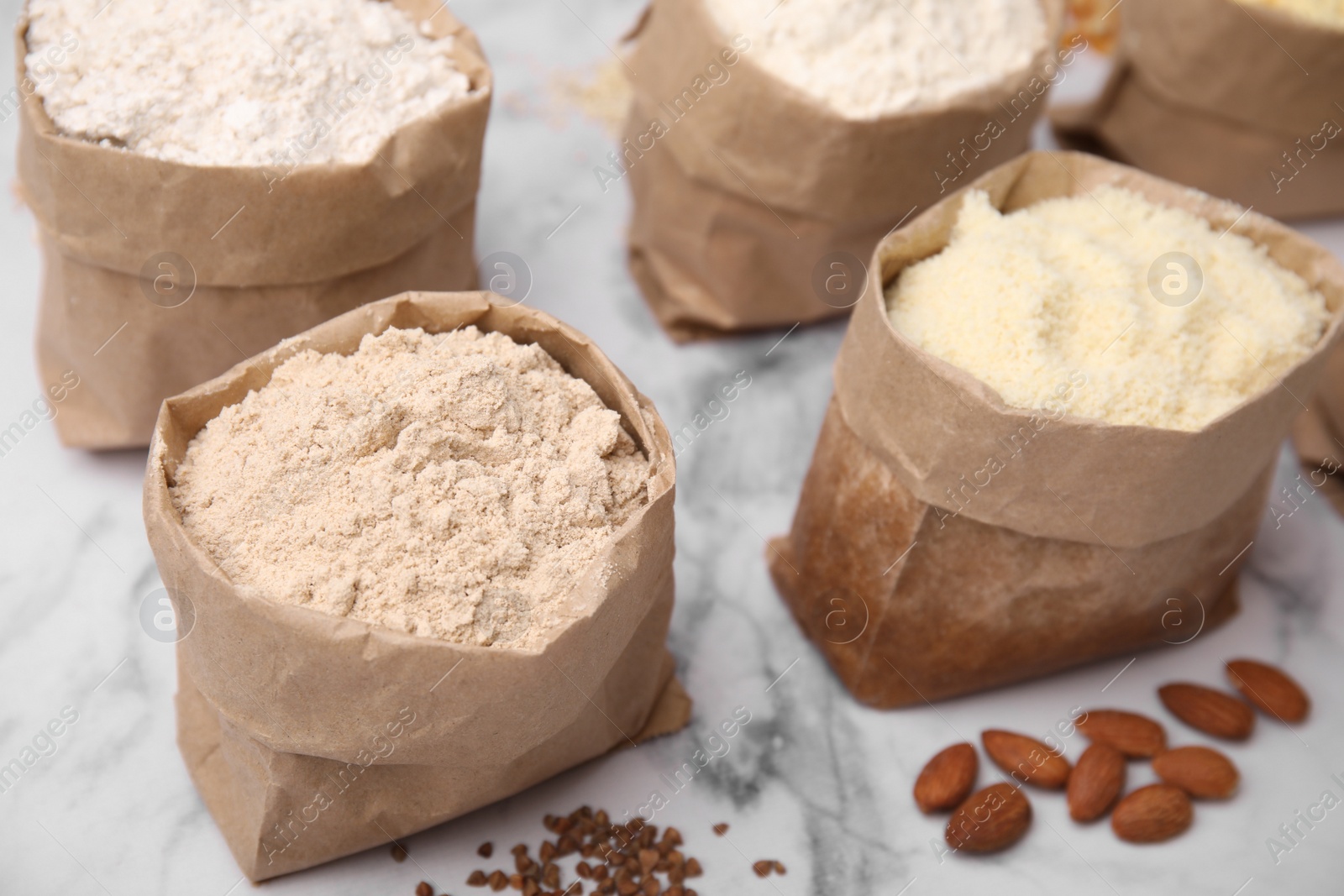 Photo of Paper bags with different types of flour and ingredients on white marble table