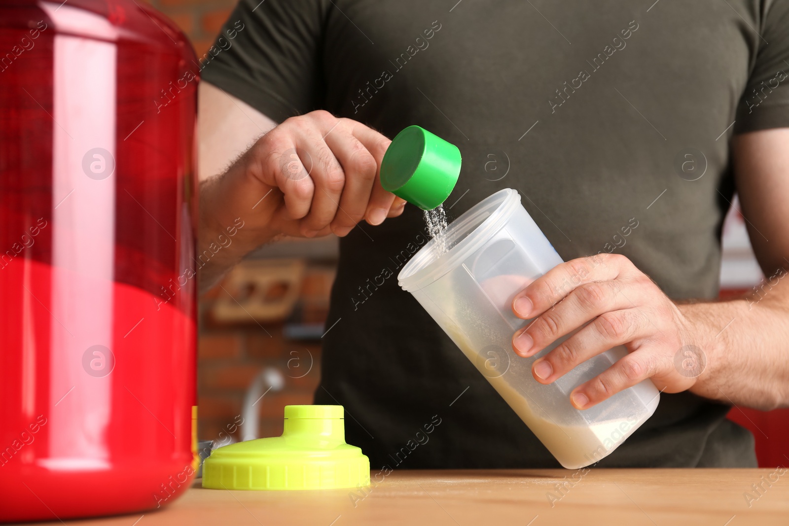 Photo of Man preparing protein shake at wooden table in kitchen, closeup