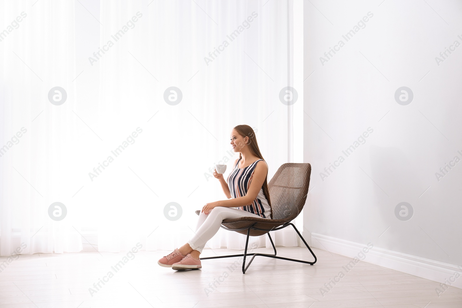 Photo of Young woman with cup of hot drink sitting in armchair at home. Space for text