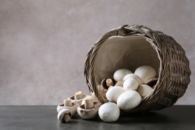Photo of Fresh champignon mushrooms scattered from basket on table. Space for text