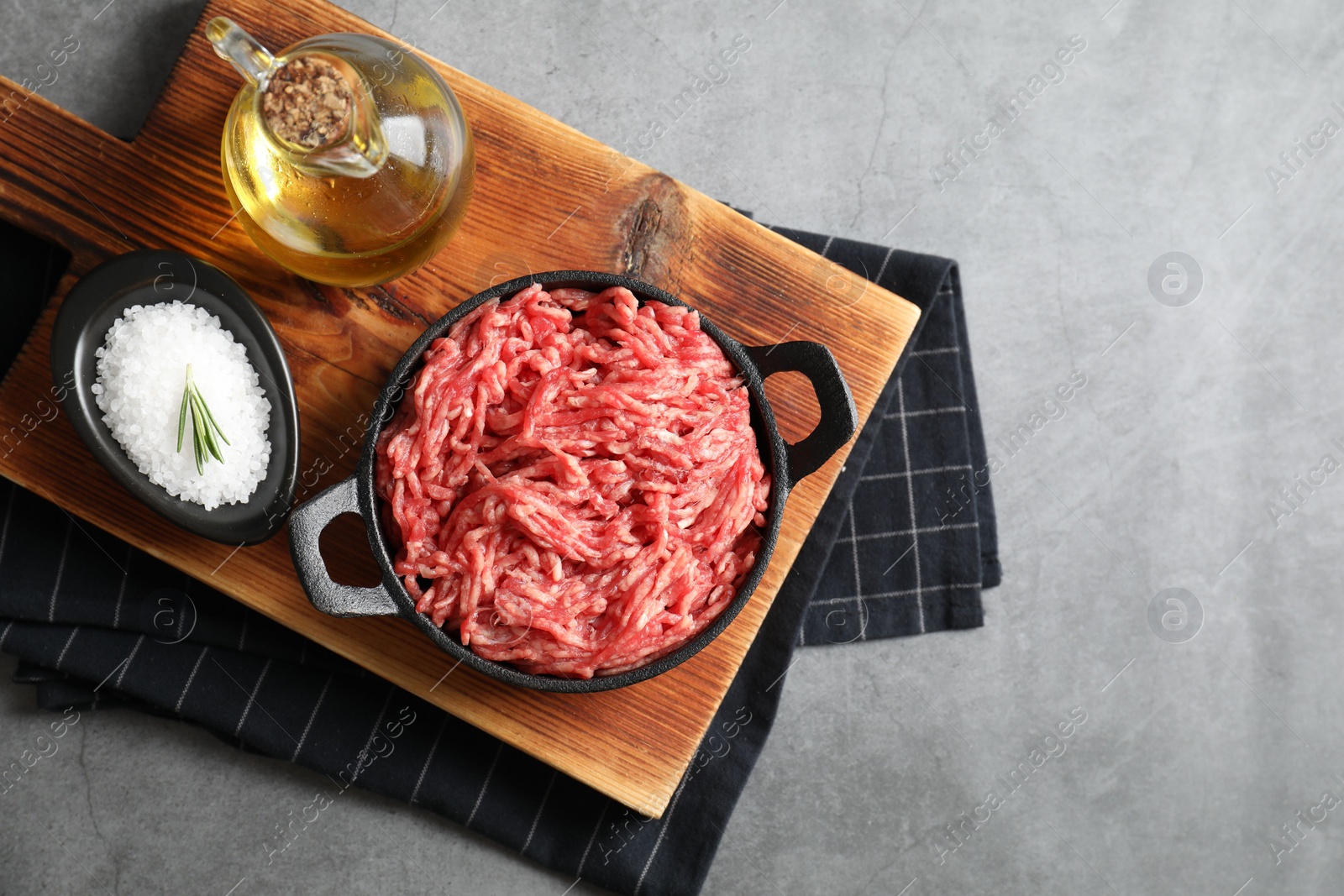 Photo of Raw ground meat in bowl, salt and oil on grey table, top view. Space for text