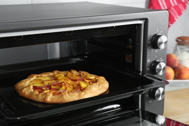 Photo of Open electric oven with delicious pie on table