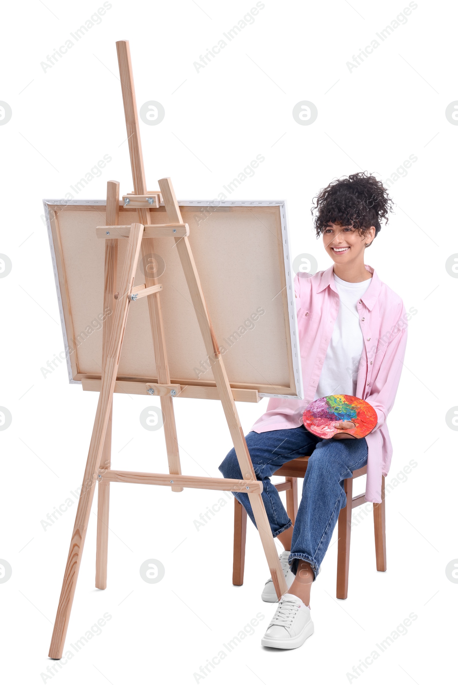 Photo of Young woman painting on easel with canvas against white background