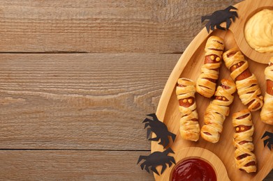Photo of Cute sausage mummies served with sauce on wooden table, top view with space for text. Halloween party food
