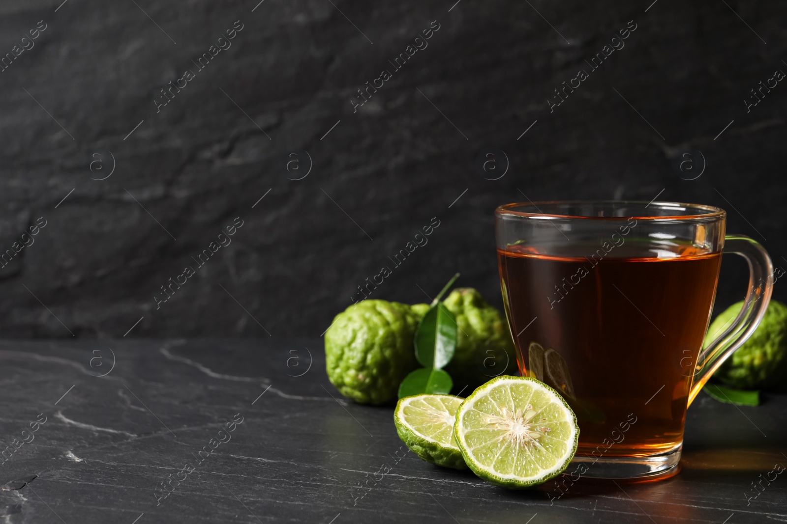 Photo of Glass cup of tasty bergamot tea and fresh fruits on black table, space for text