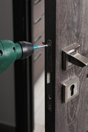 Photo of Repairing door handle with electric screwdriver indoors, closeup