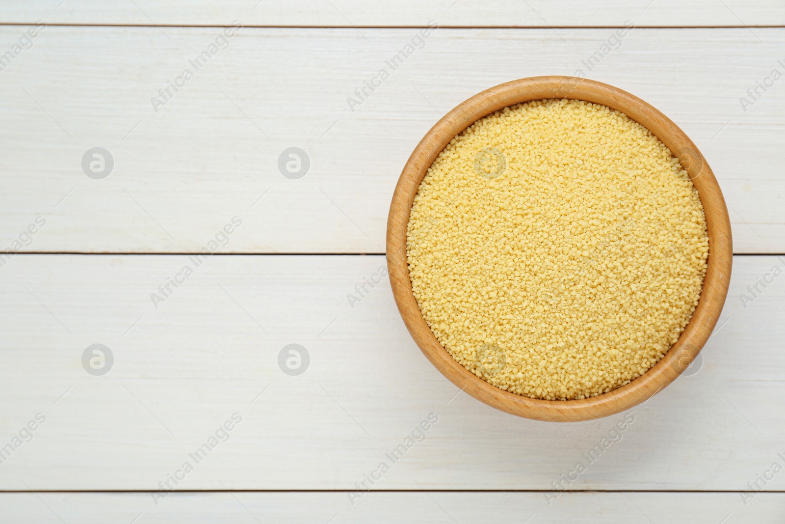 Photo of Bowl of raw couscous on white wooden table, top view. Space for text