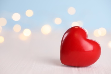 Red heart on white wooden table against festive lights, space for text. St. Valentine's day