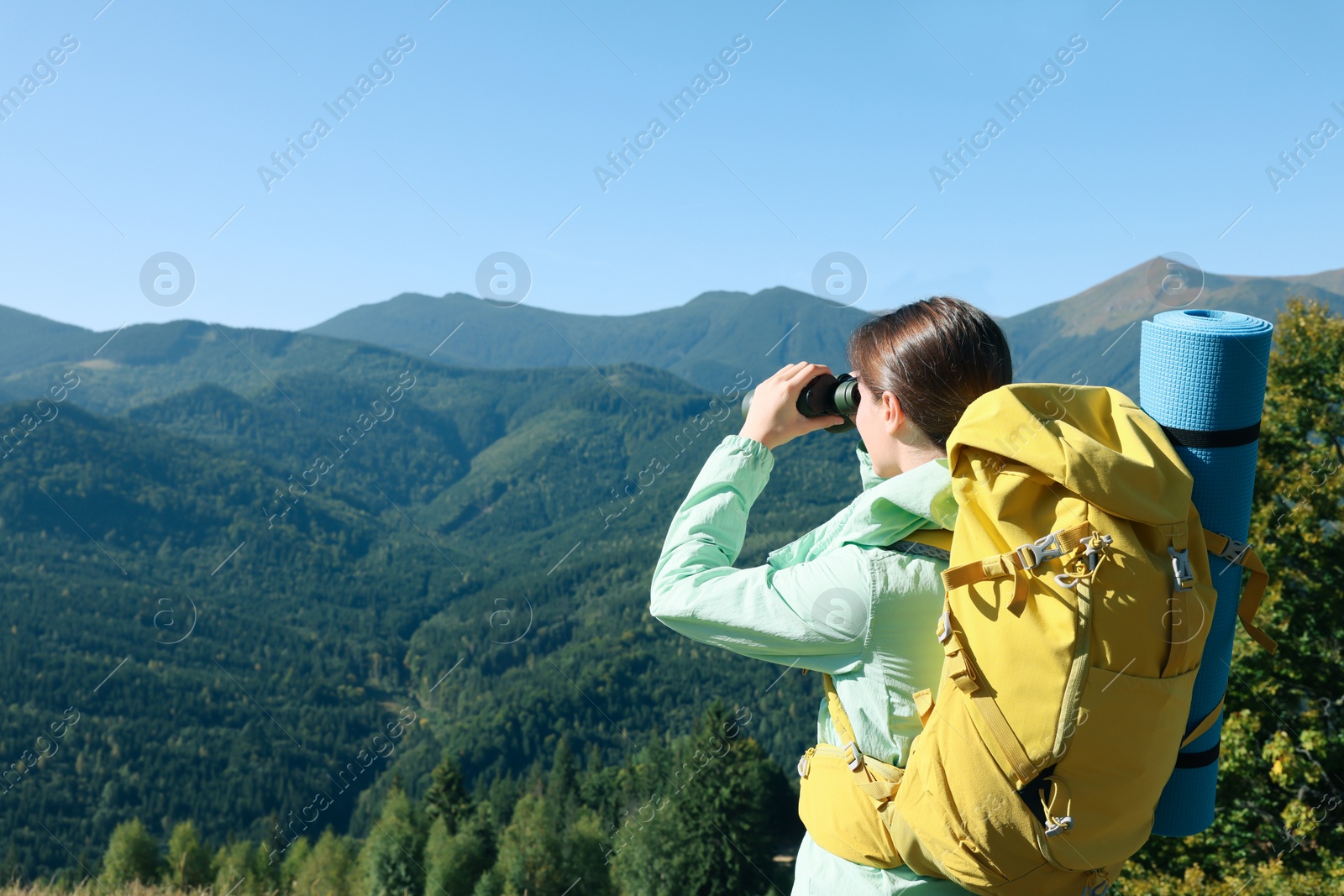 Photo of Tourist with hiking equipment looking through binoculars in mountains