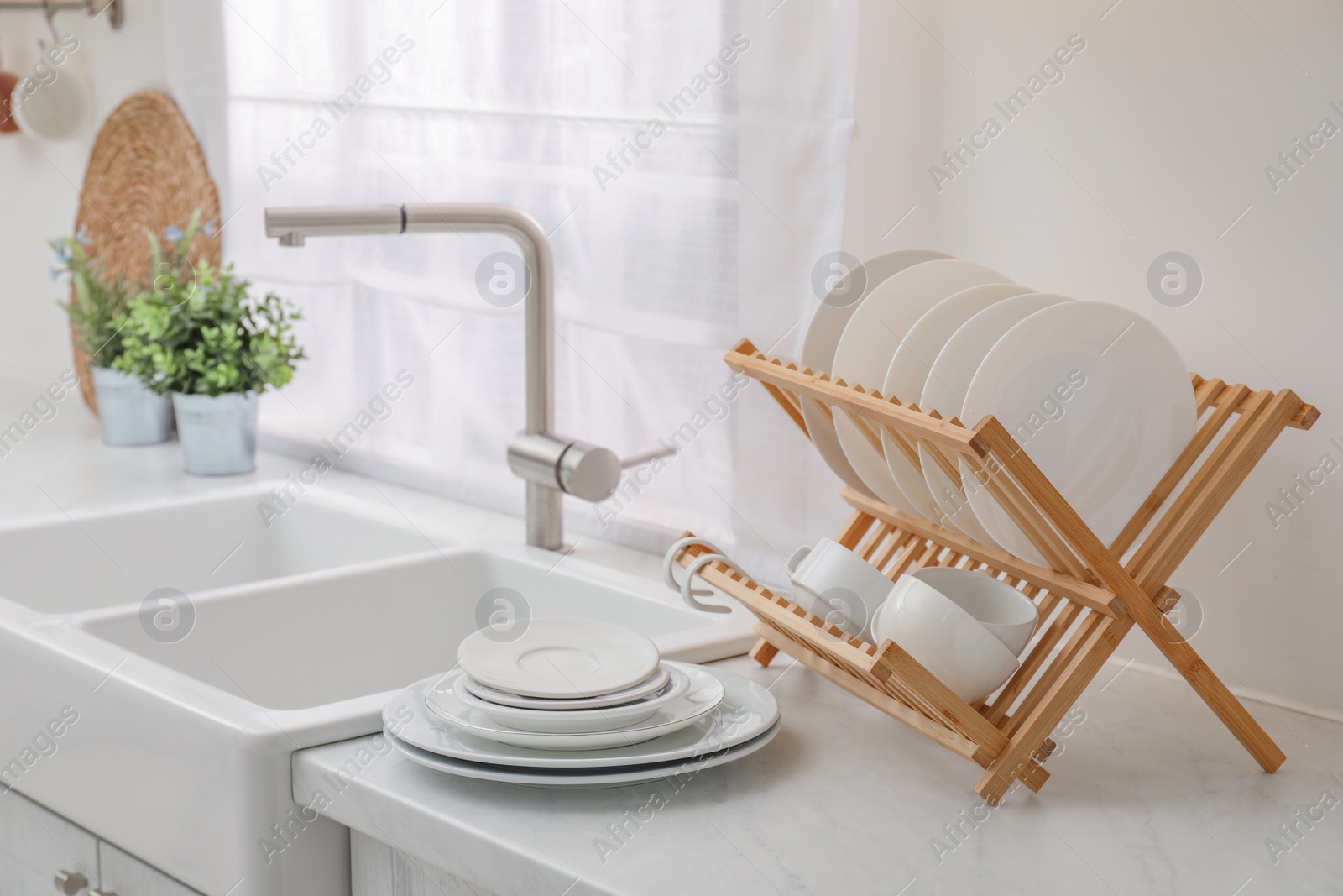 Photo of Drying rack with clean dishes on light marble countertop near sink in kitchen