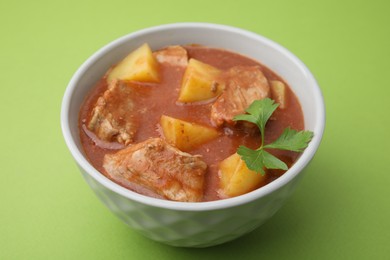 Delicious goulash in bowl on green background