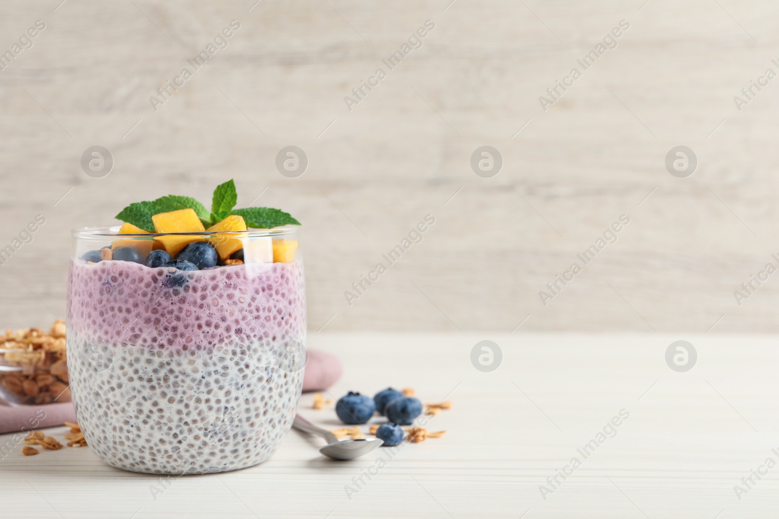 Photo of Delicious chia pudding with blueberries, mango and mint on white wooden table, space for text