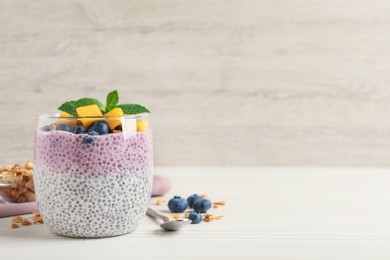 Delicious chia pudding with blueberries, mango and mint on white wooden table, space for text