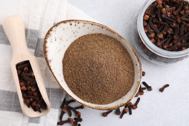 Aromatic clove powder, scoop and dried buds on light table, flat lay