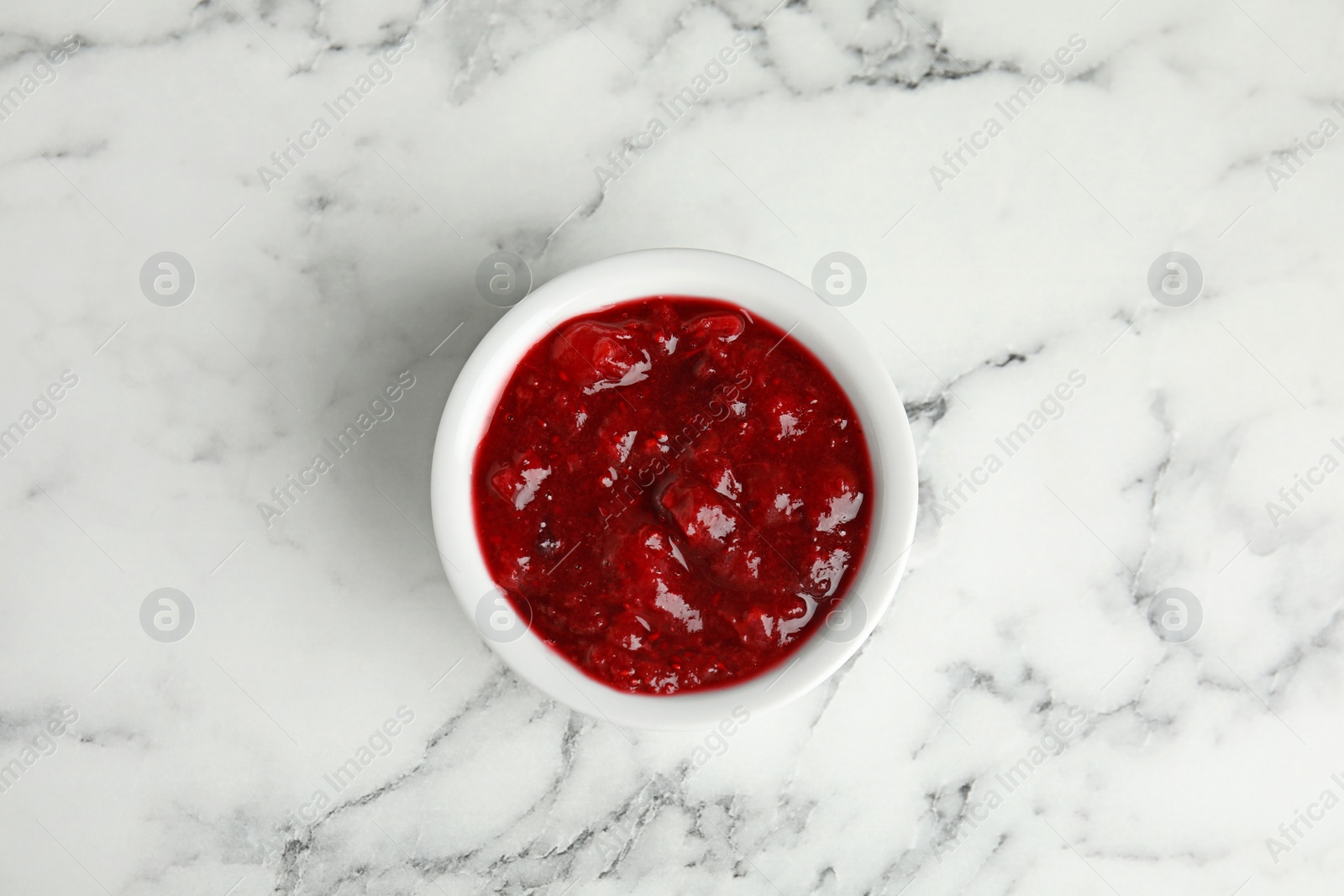 Photo of Bowl of cranberry sauce on marble background, top view