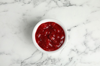 Photo of Bowl of cranberry sauce on marble background, top view