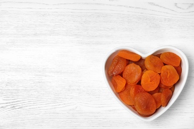 Photo of Bowl of dried apricots on white wooden table, top view with space for text. Healthy fruit