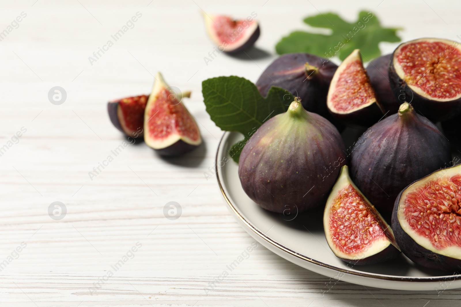 Photo of Whole and cut ripe figs on white wooden table, closeup. Space for text