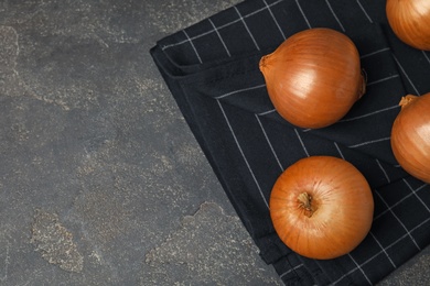 Photo of Black fabric with ripe onions on grey table, flat lay. Space for text