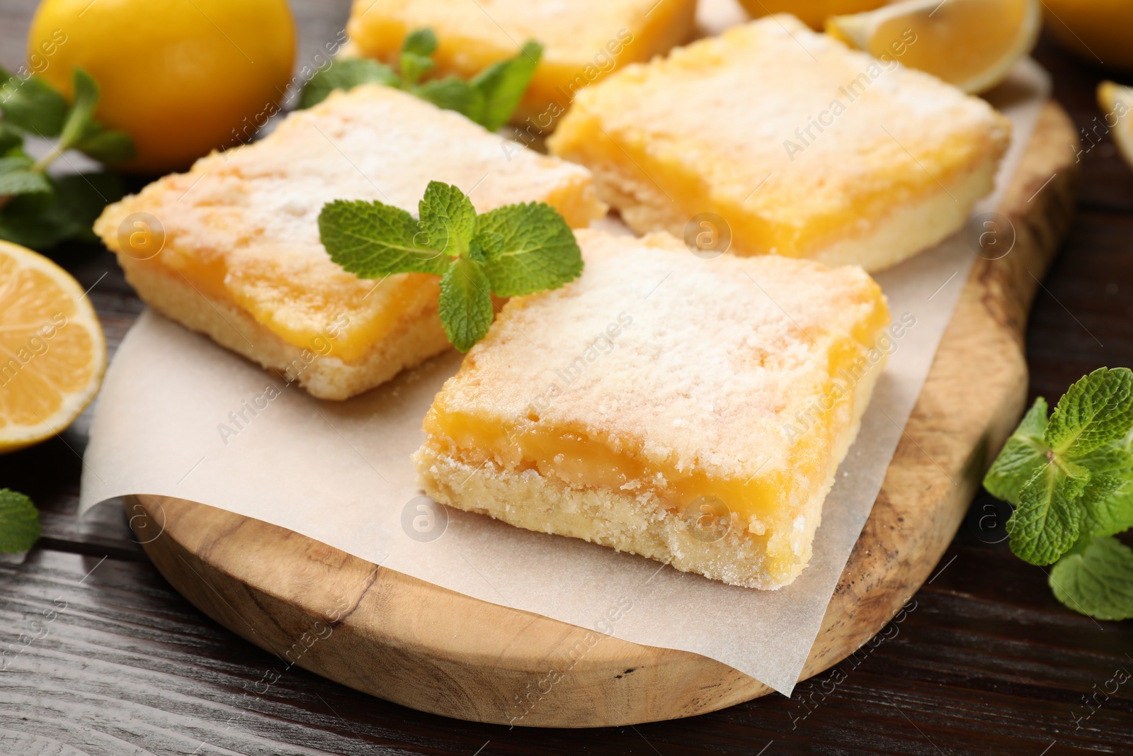 Photo of Tasty lemon bars with powdered sugar and mint on wooden table, closeup