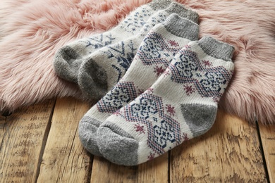 Photo of Knitted socks and pink faux fur on wooden table, closeup