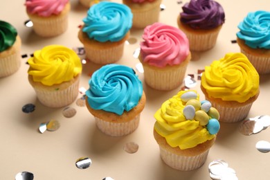 Delicious cupcakes with bright cream and confetti on beige background, closeup