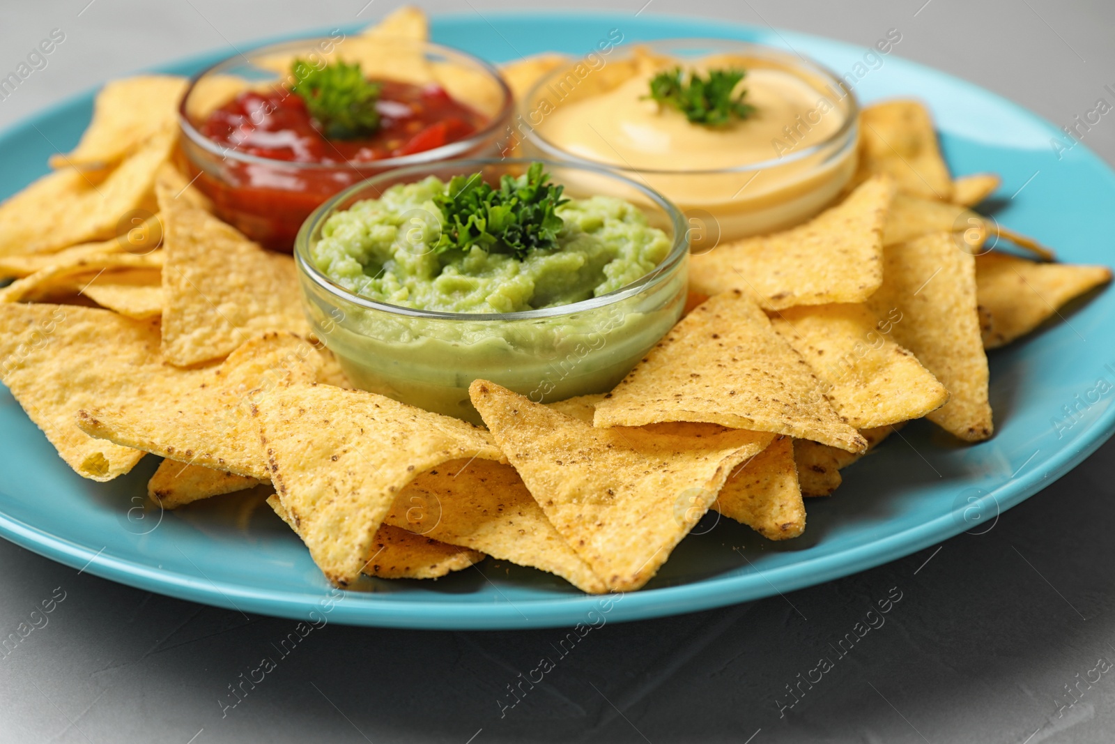 Photo of Blue plate with tasty Mexican nachos chips and sauces on grey table, closeup view