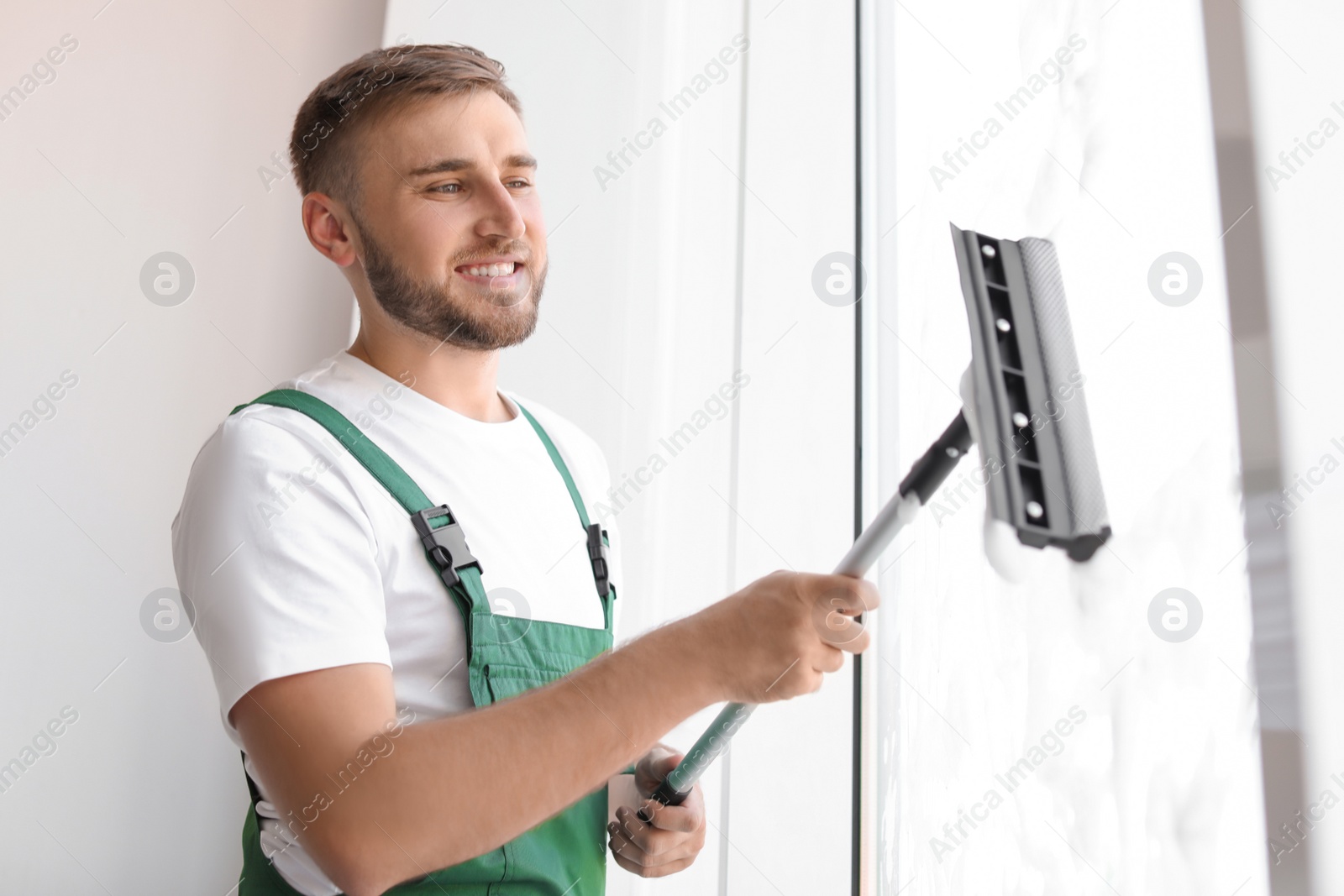 Photo of Male cleaner wiping window glass with squeegee indoors