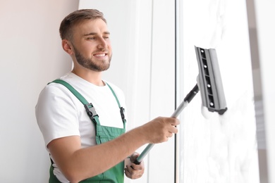 Male cleaner wiping window glass with squeegee indoors