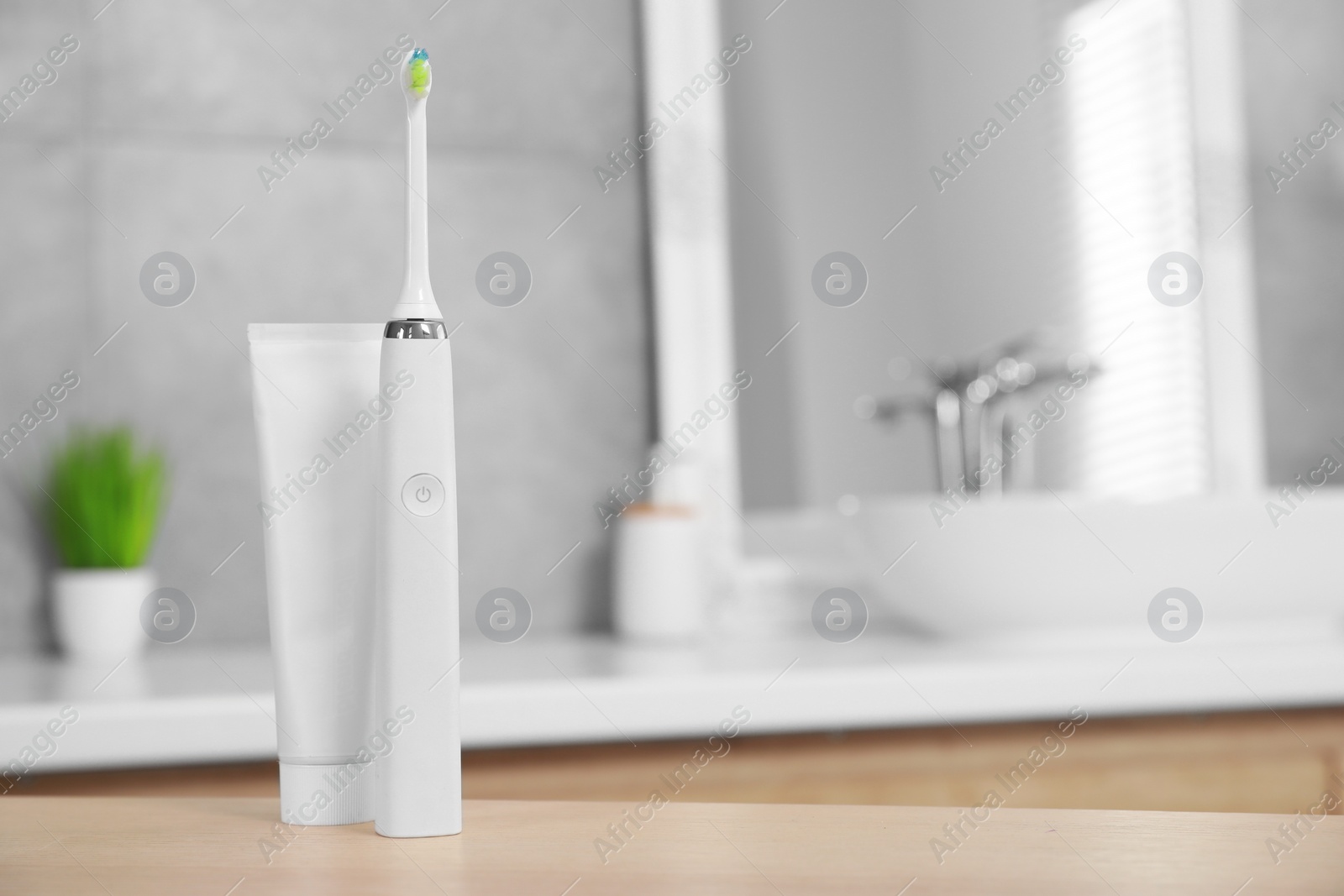 Photo of Electric toothbrush and tube with paste on wooden table in bathroom. Space for text