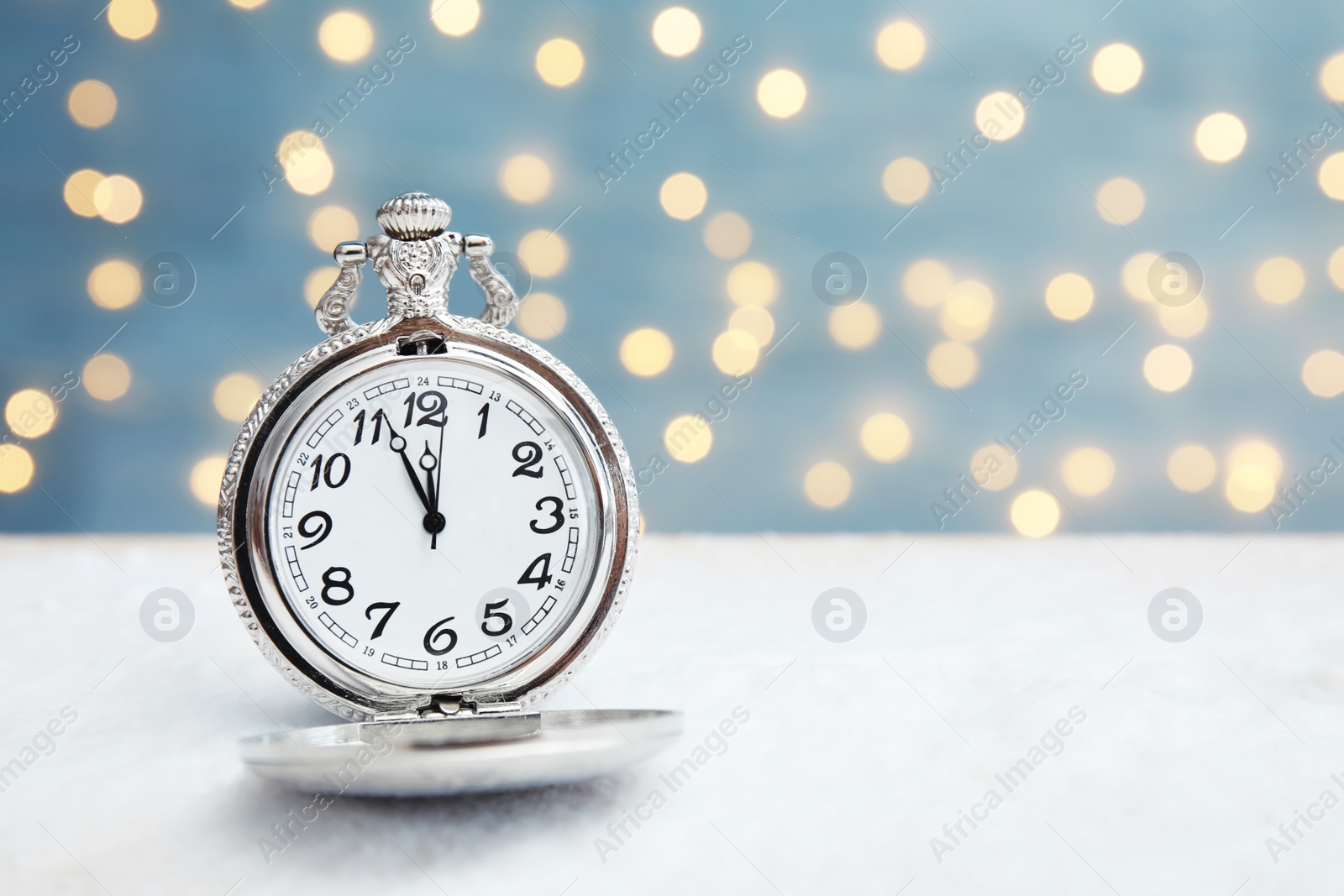 Photo of Pocket watch with snow on table against blurred lights. Christmas countdown