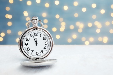 Pocket watch with snow on table against blurred lights. Christmas countdown