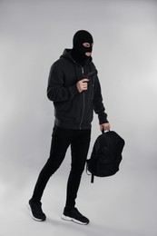 Man wearing black balaclava with backpack and gun on light grey background