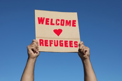 Image of Man holding poster with phrase WELCOME REFUGEES outdoors, closeup