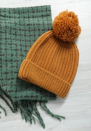 Photo of Soft green scarf and knitted hat on white wooden table, top view