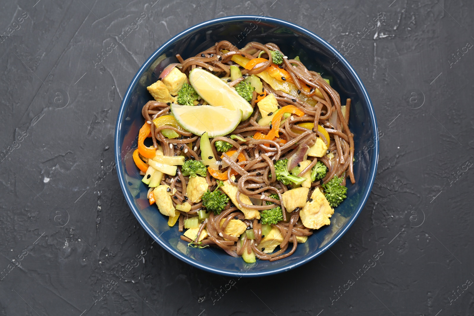 Photo of Stir-fry. Delicious cooked noodles with chicken and vegetables in bowl on gray textured table, top view