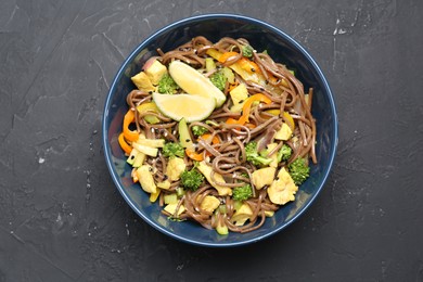 Photo of Stir-fry. Delicious cooked noodles with chicken and vegetables in bowl on gray textured table, top view