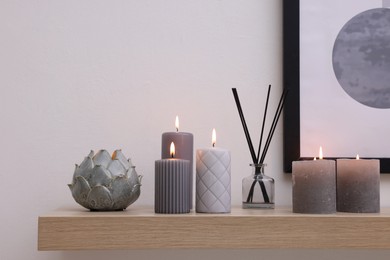 Photo of Burning candles and air freshener on wooden shelf indoors