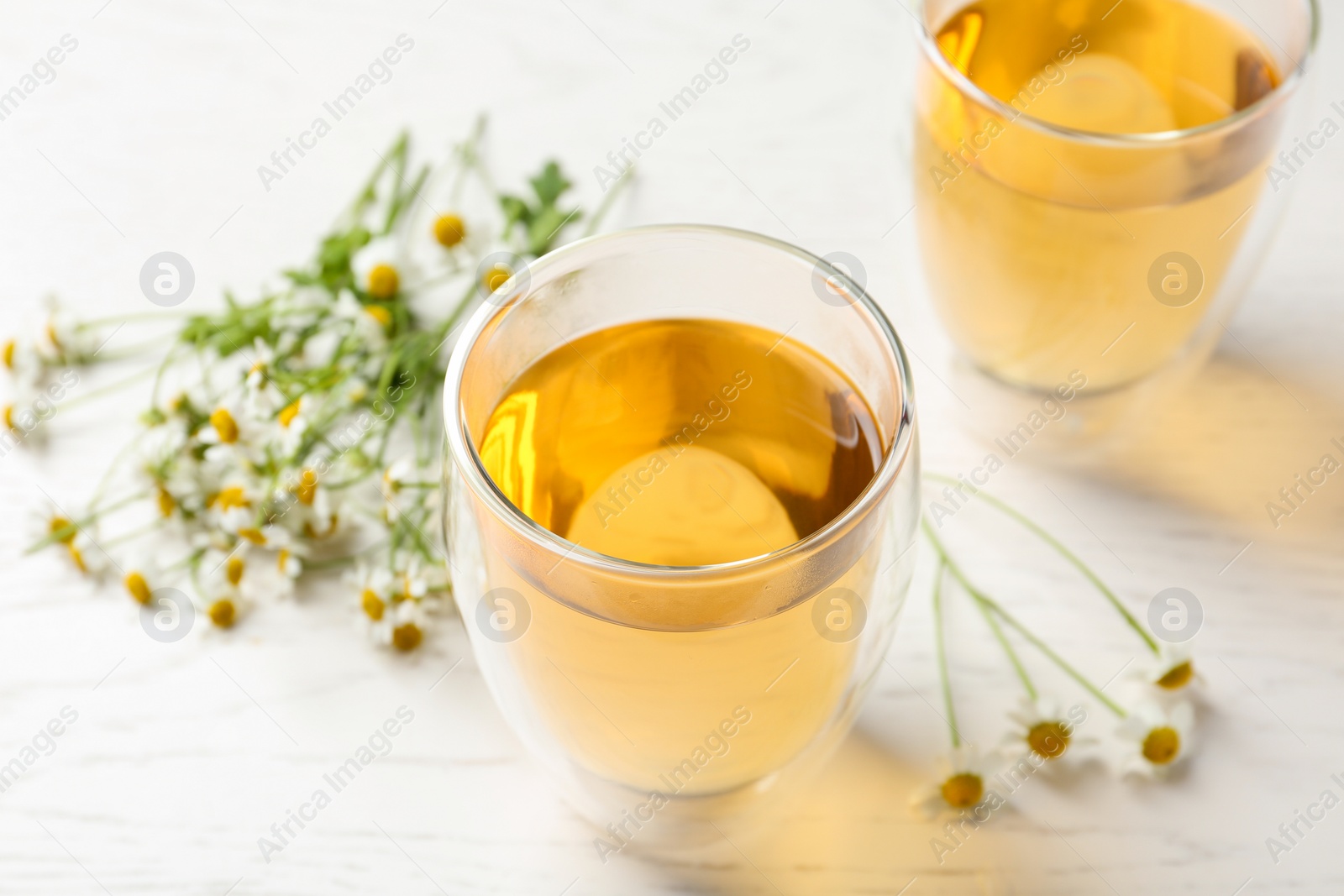 Photo of Delicious chamomile tea in glass on white table