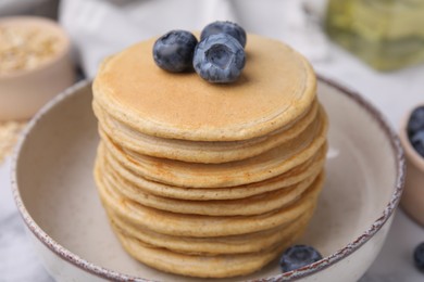 Photo of Tasty oatmeal pancakes with blueberries in bowl, closeup