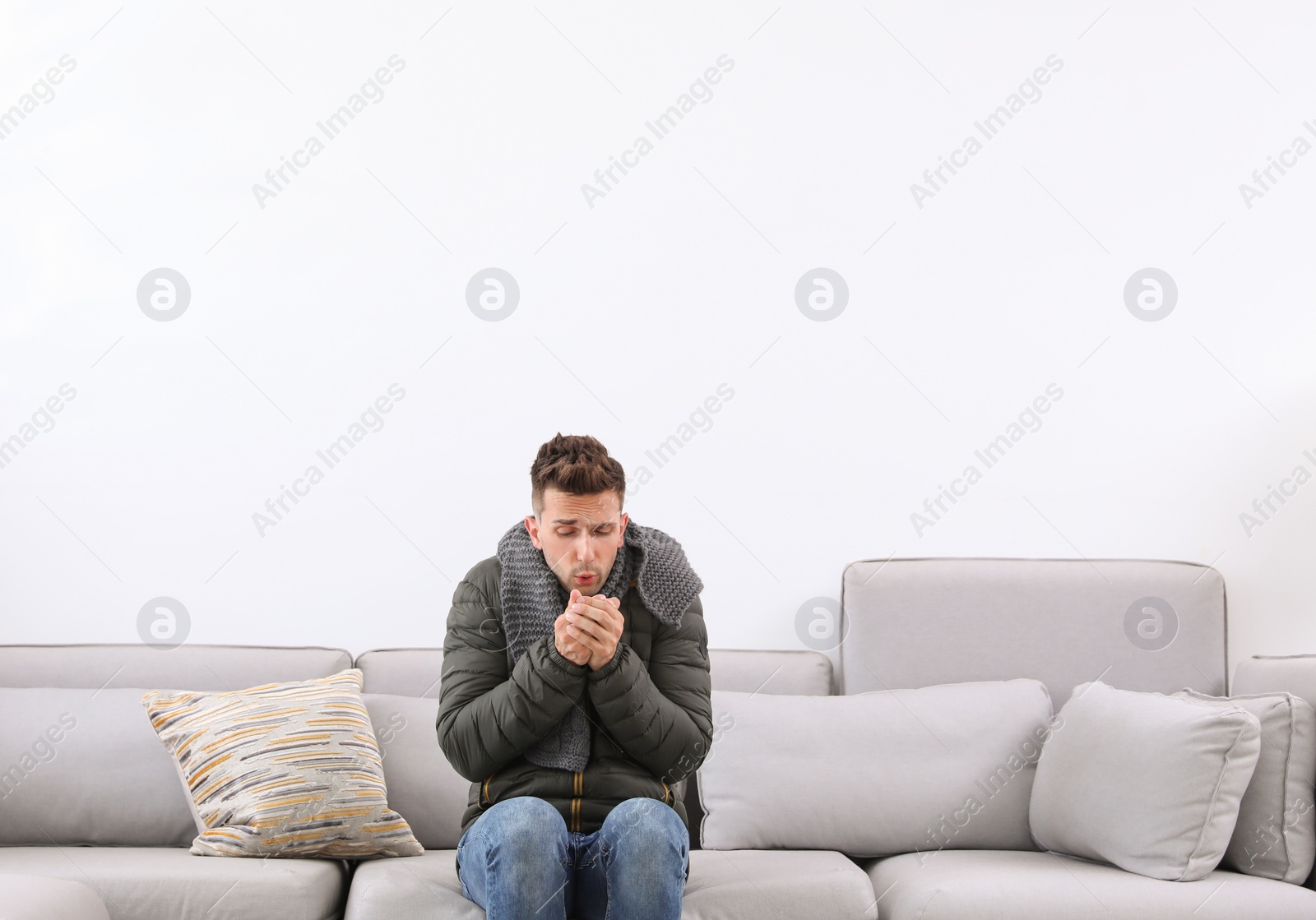 Photo of Young man wearing warm clothes freezing on sofa at home. Air conditioner malfunction