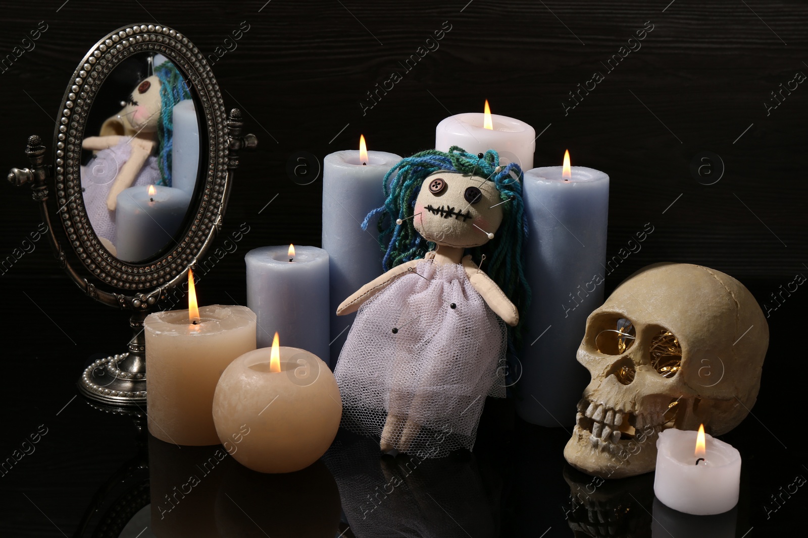 Photo of Voodoo doll pierced with pins and candles on black table. Curse ceremony