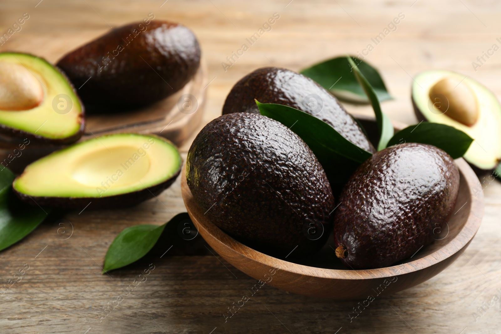 Photo of Whole and cut avocados on wooden table, closeup