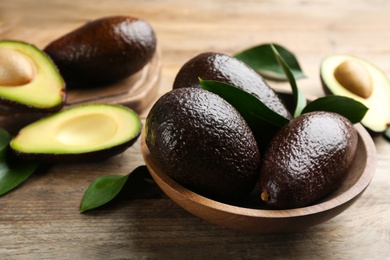 Whole and cut avocados on wooden table, closeup
